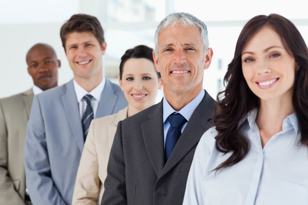 Five smiling employees standing around their manager